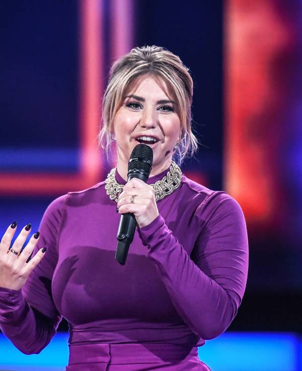 Beatrice Egli moderiert in einem lila Kleid auf der Bühne.