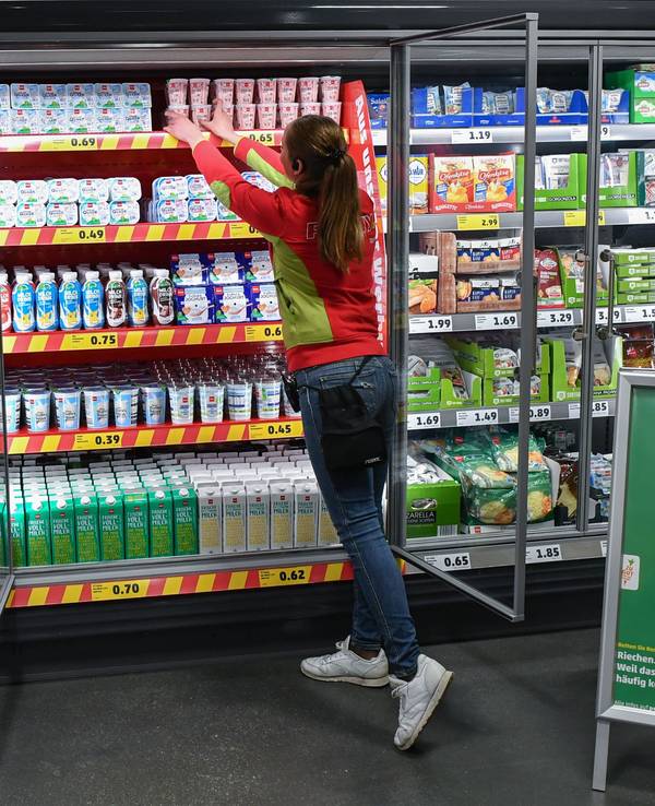 Ein Mitarbeitern ordnet die Milchprodukte in einem Kühlregal im Lebensmittel-Discounter Penny, vor dem der Aufsteller mit der Werbung der Kampagne «Kostbares retten» steht.