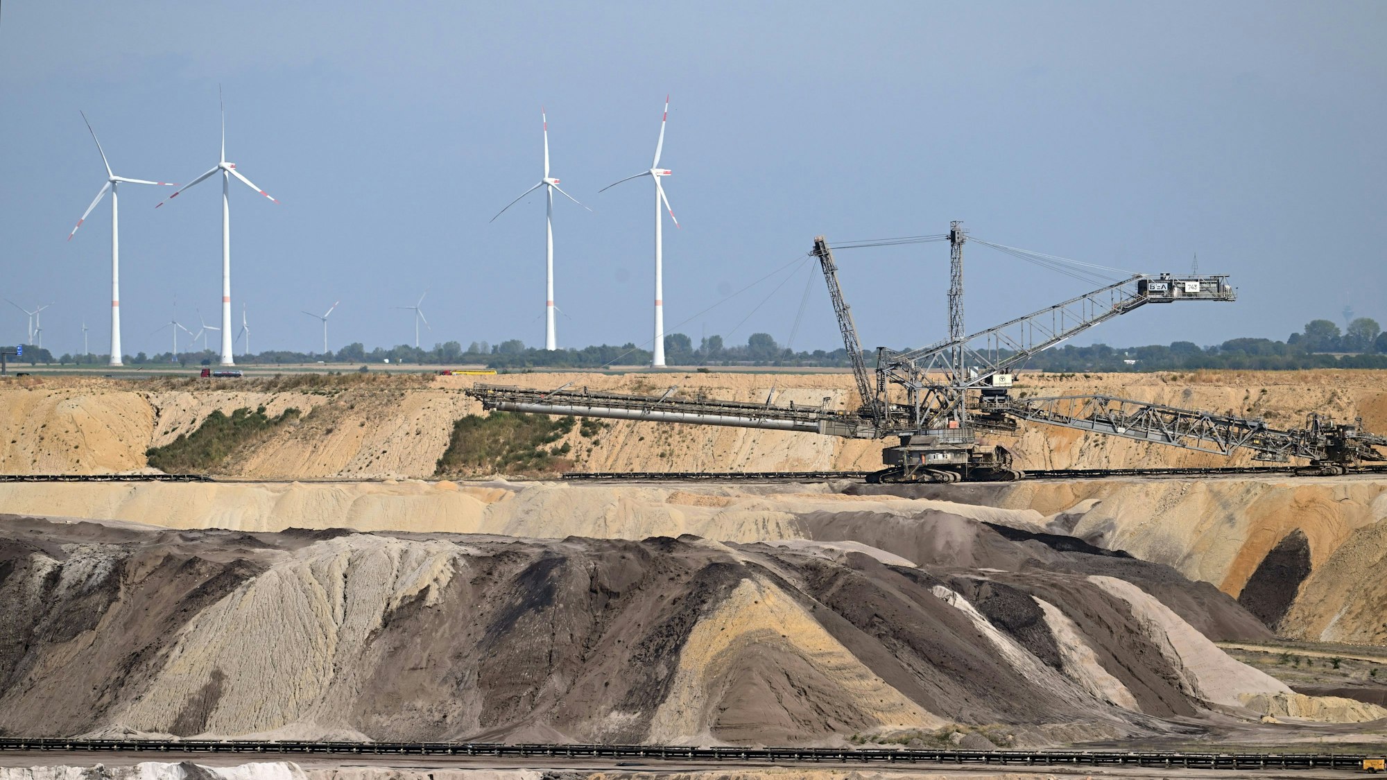 Ein Schaufelradbagger arbeitet im Braunkohletagebau Garzweiler. Im Hintergrund sind Windräder zu sehen. Das Foto stammt aus dem September 2022.