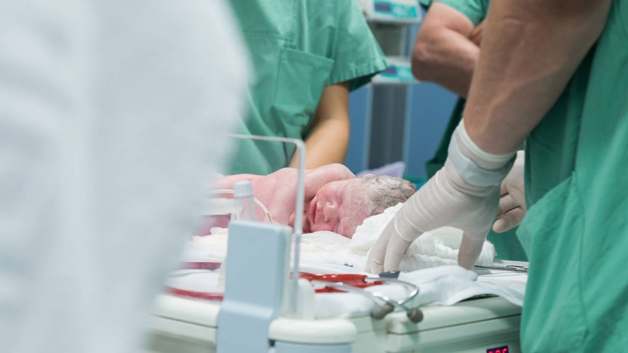 Das Symbolfoto aus dem Jahr 2016 zeigt ein Neugeborenes, das von Krankenhauspersonal in grünen Kitteln umgeben ist.