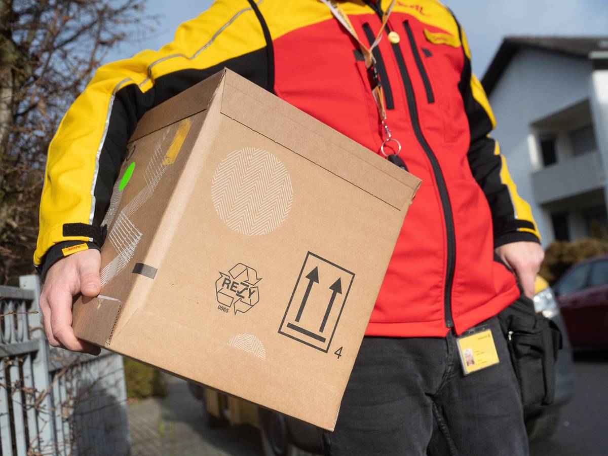 Das Symbolfoto zeigt einen DHL-Mitarbeiter mit einem Paket unter dem Arm.