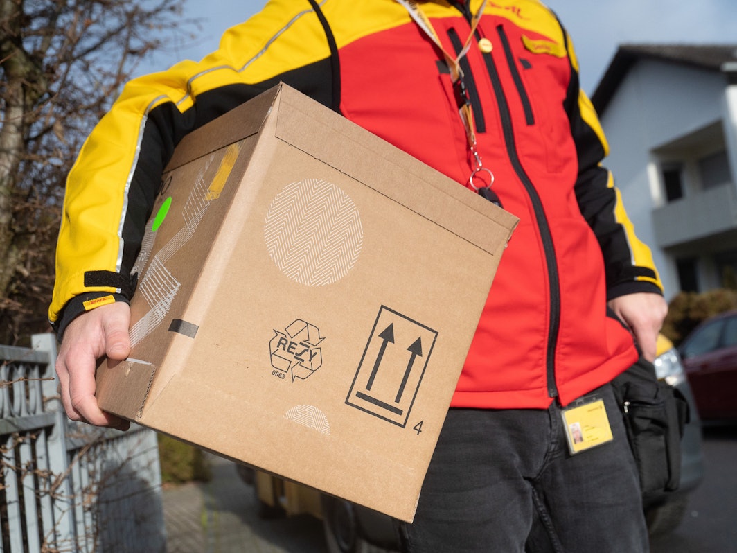 Das Symbolfoto zeigt einen DHL-Mitarbeiter mit einem Paket unter dem Arm.