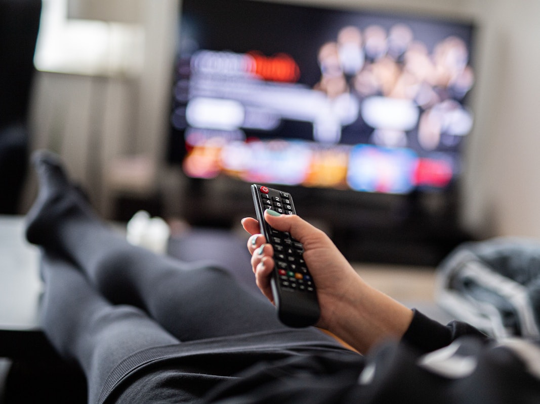 Eine Frau sitzt vor dem Fernseher und hält die Fernbedienung.