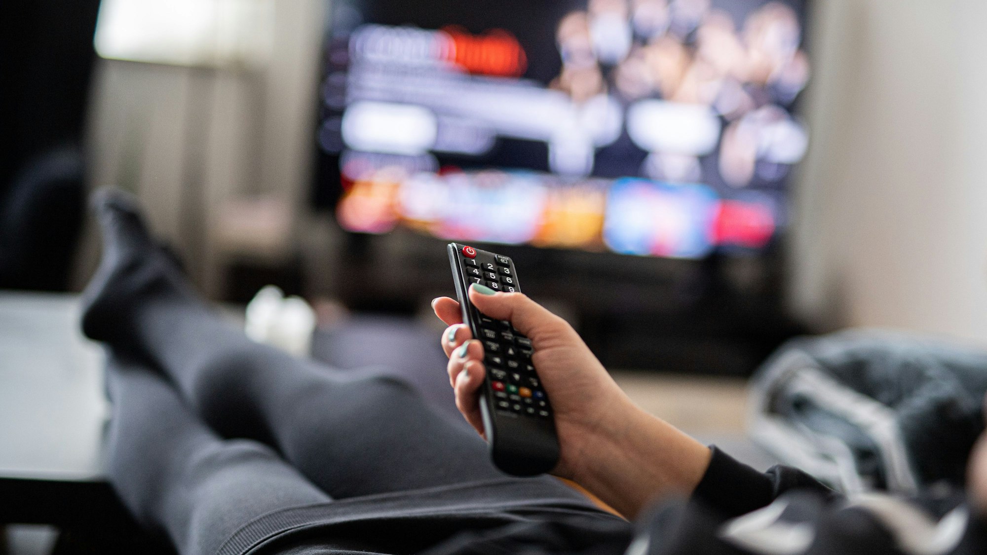 Eine Frau sitzt vor dem Fernseher und hält die Fernbedienung.