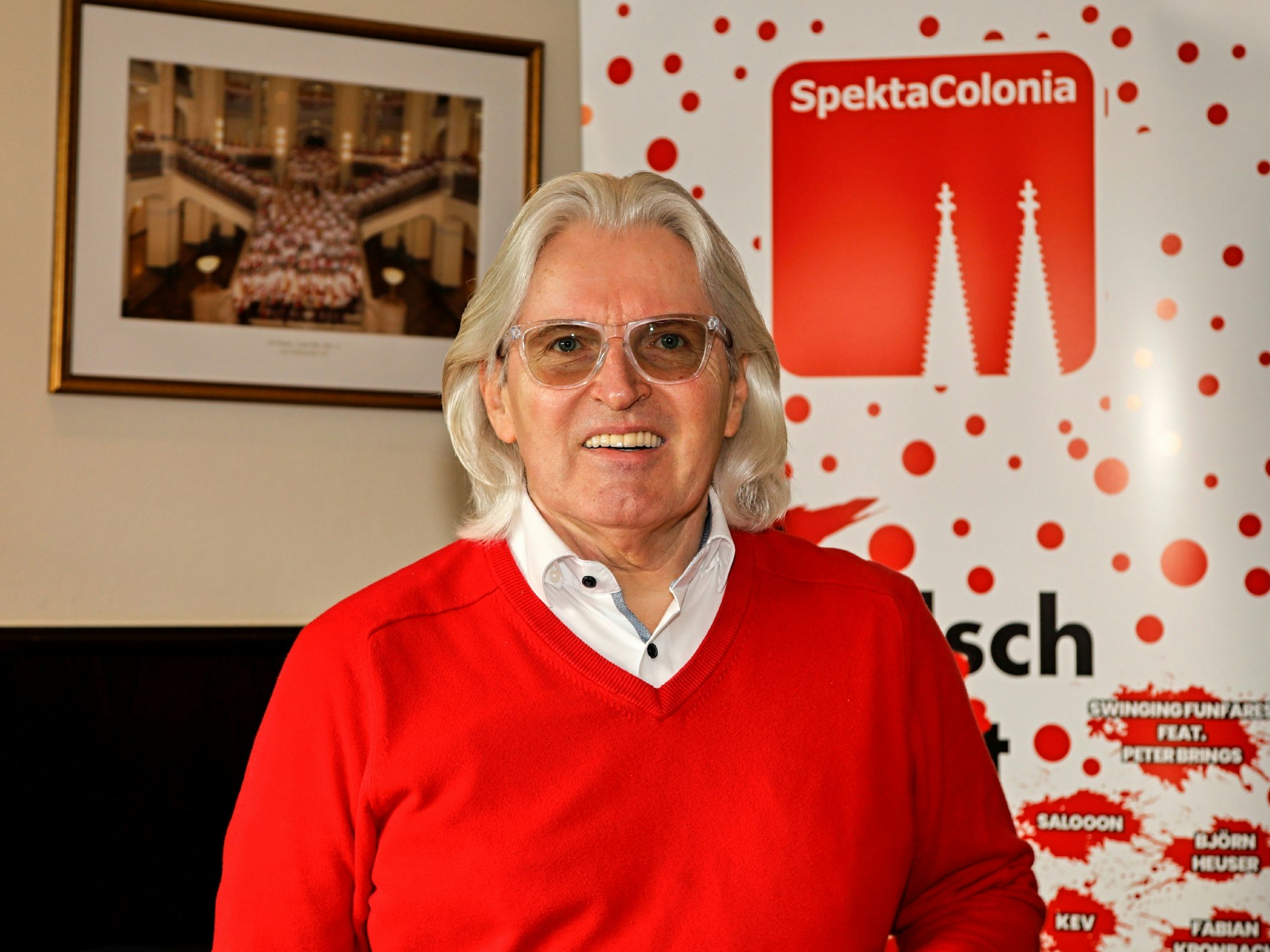 Jürgen Hoppe lächelt vor einem Schild von Spectacolonia in die Kamera.