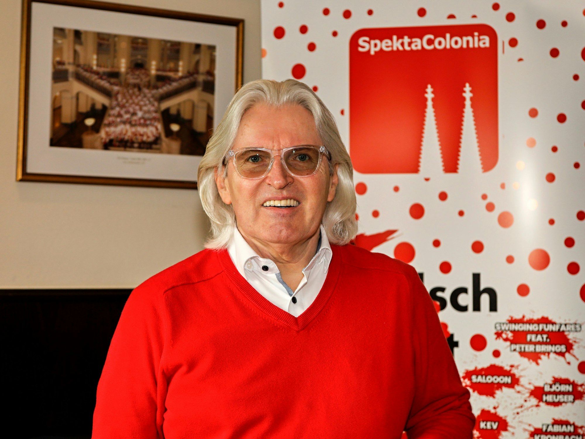 Jürgen Hoppe lächelt vor einem Schild von Spectacolonia in die Kamera.