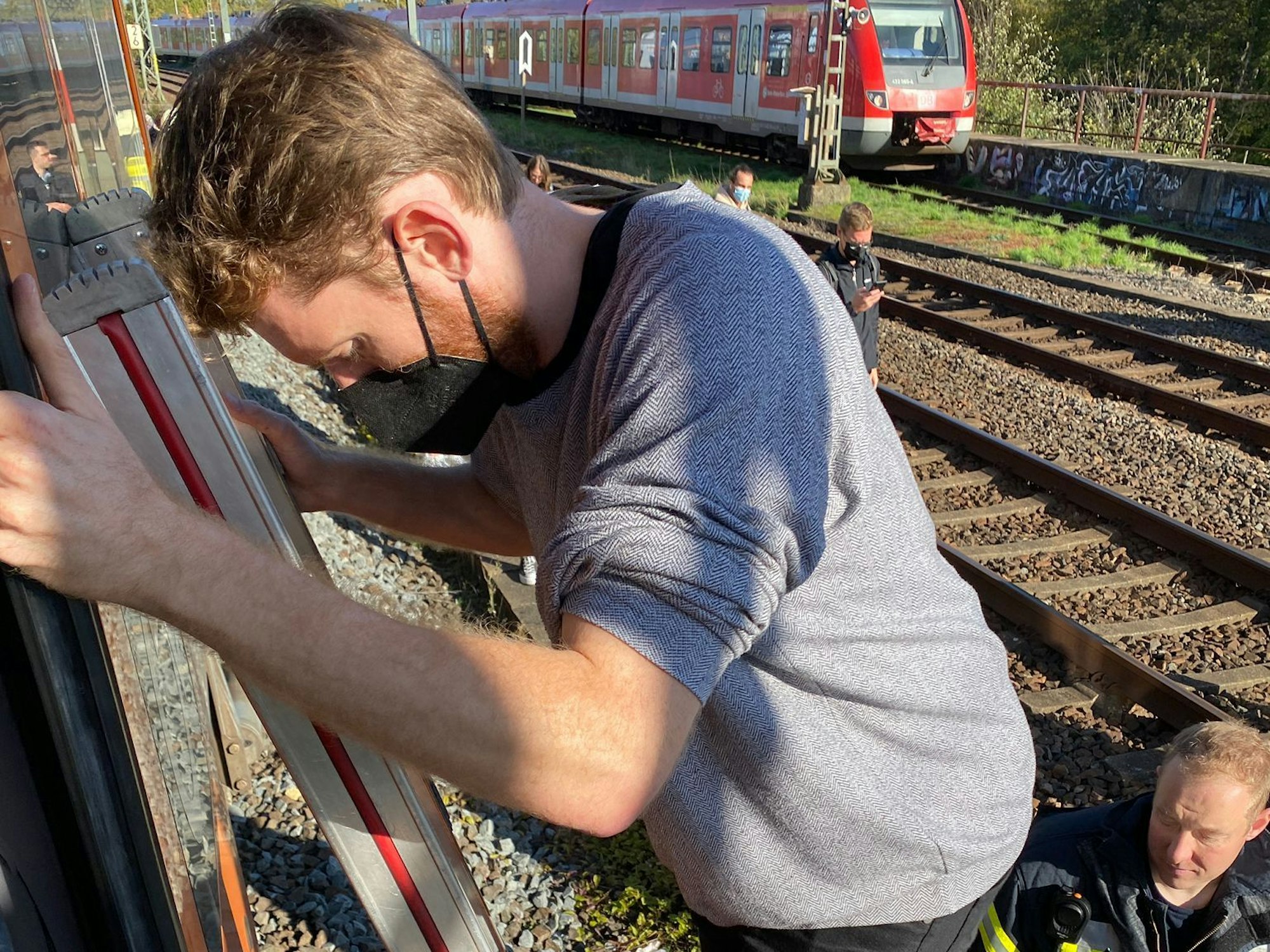 Ein Mann steigt über eine Leiter aus einem stehenden Zug auf die Gleise. Er wird von der Feuerwehr unterstützt.
