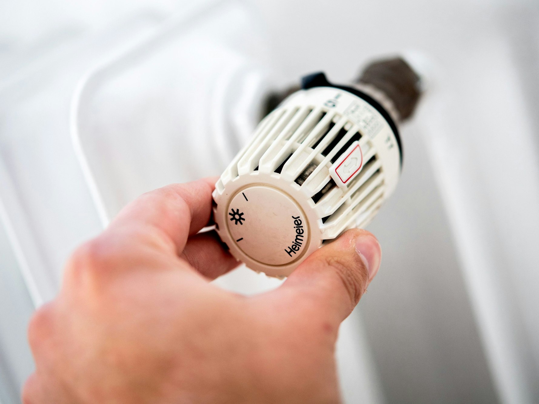 Ein Mann dreht in einer Wohnung am Thermostat einer Heizung.