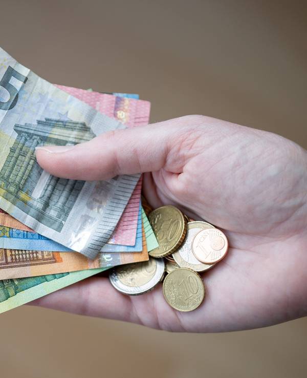Eine Frau hält Geldscheine und Münzen in der Hand.