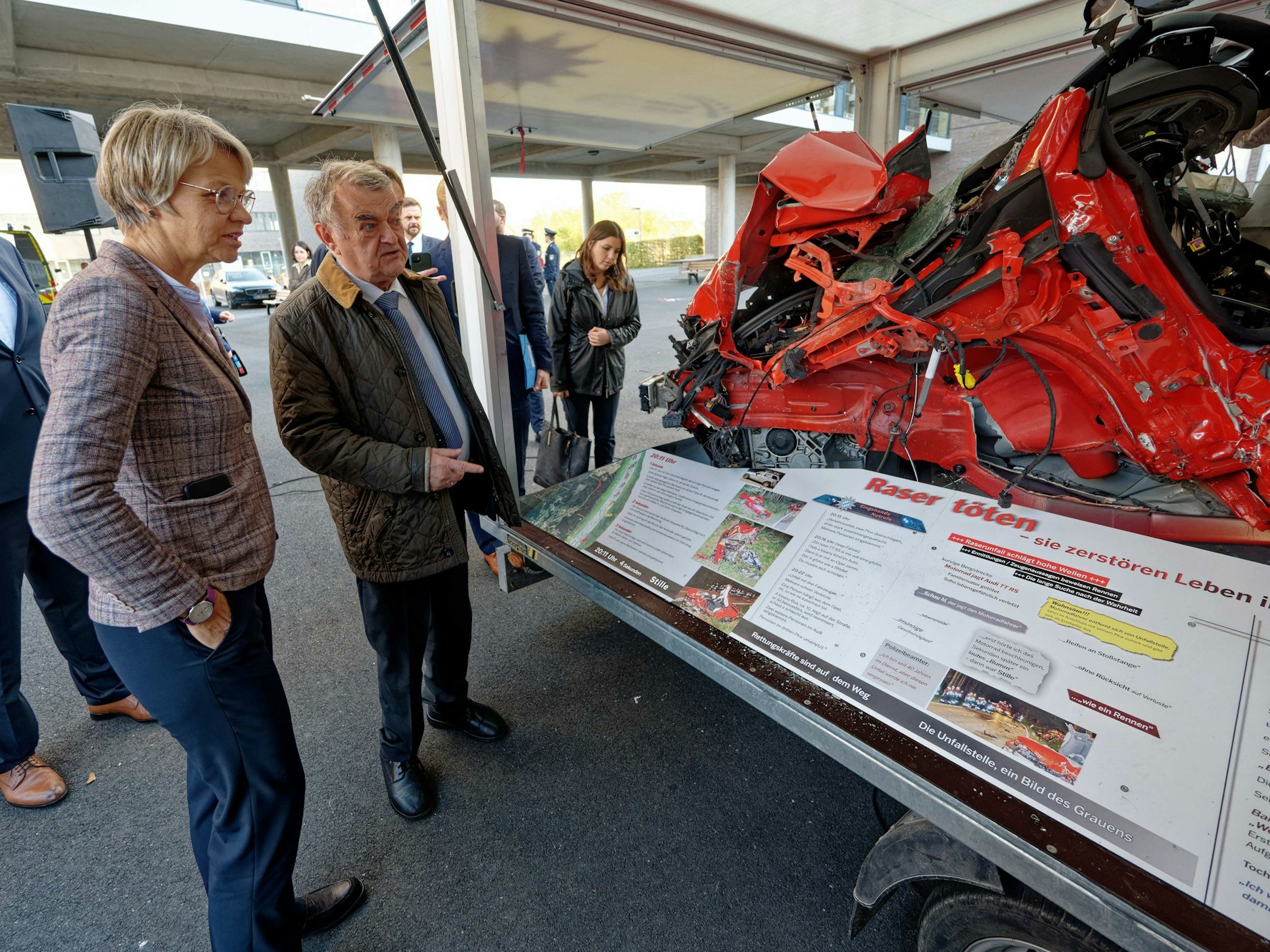 Dorothee Feller und Herbert Reul sehen sich ein völlig zerstörtes Autowrack an.