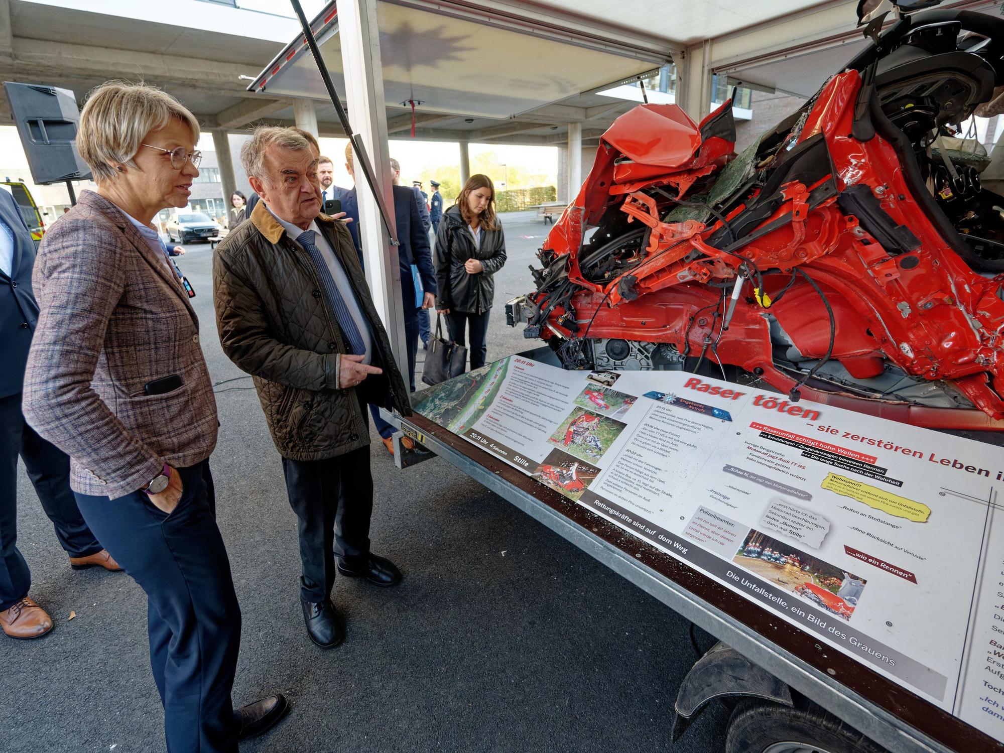 Dorothee Feller und Herbert Reul sehen sich ein völlig zerstörtes Autowrack an.