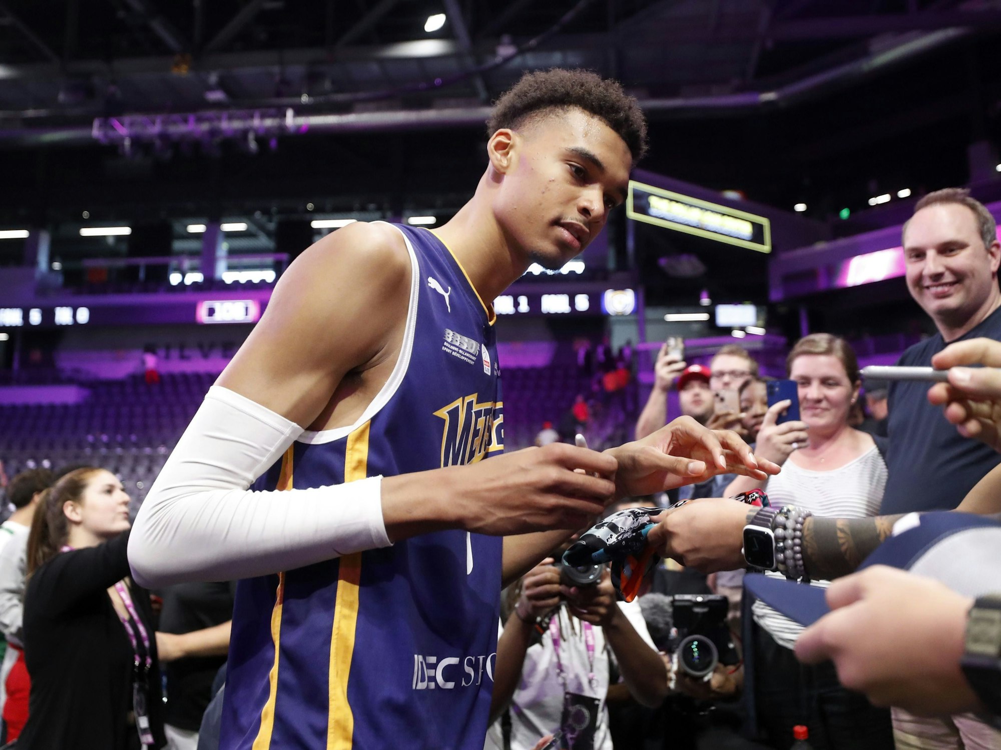 Basketballspieler Victor Wembanyama gibt in einer Halle Autogramme für Fans.