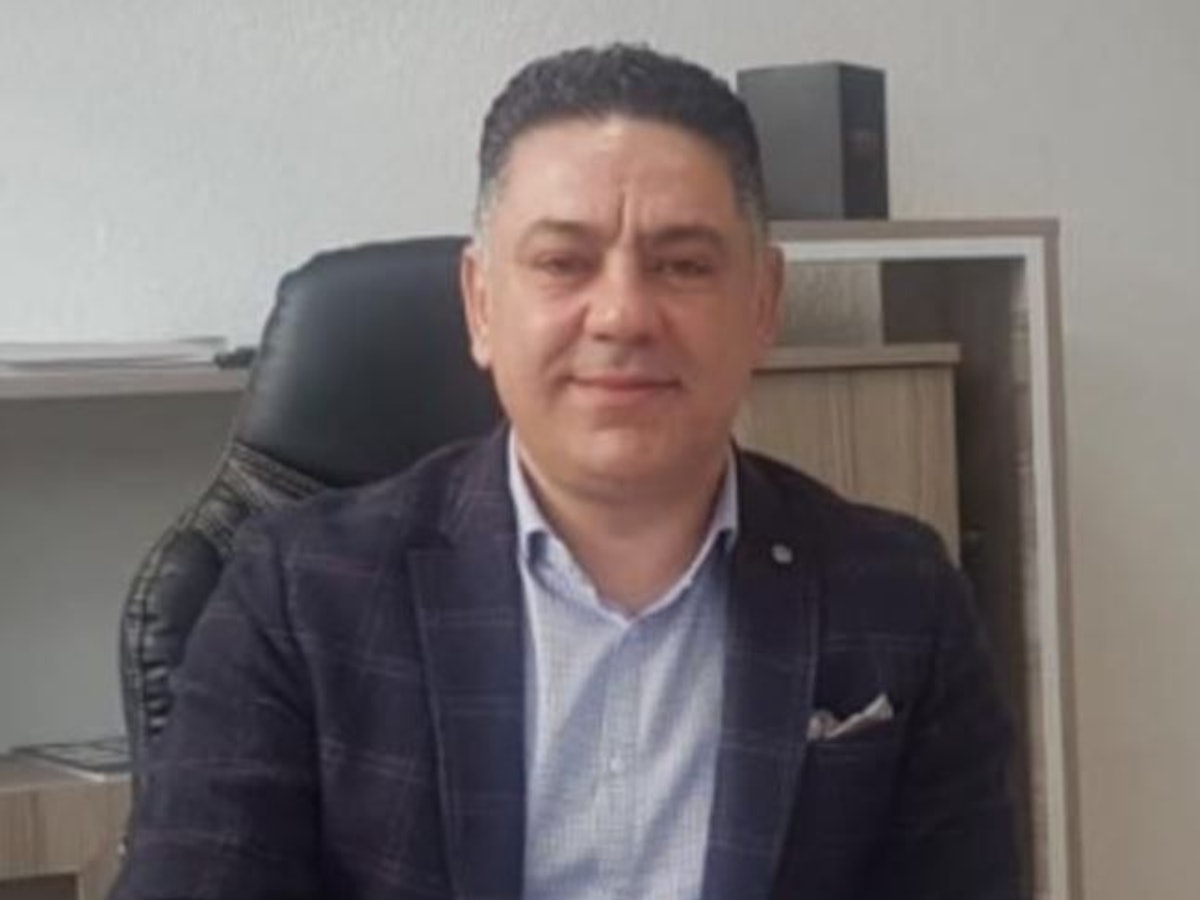 Fahndungsfoto: Ein Mann sitzt hinter einem Schreibtisch.