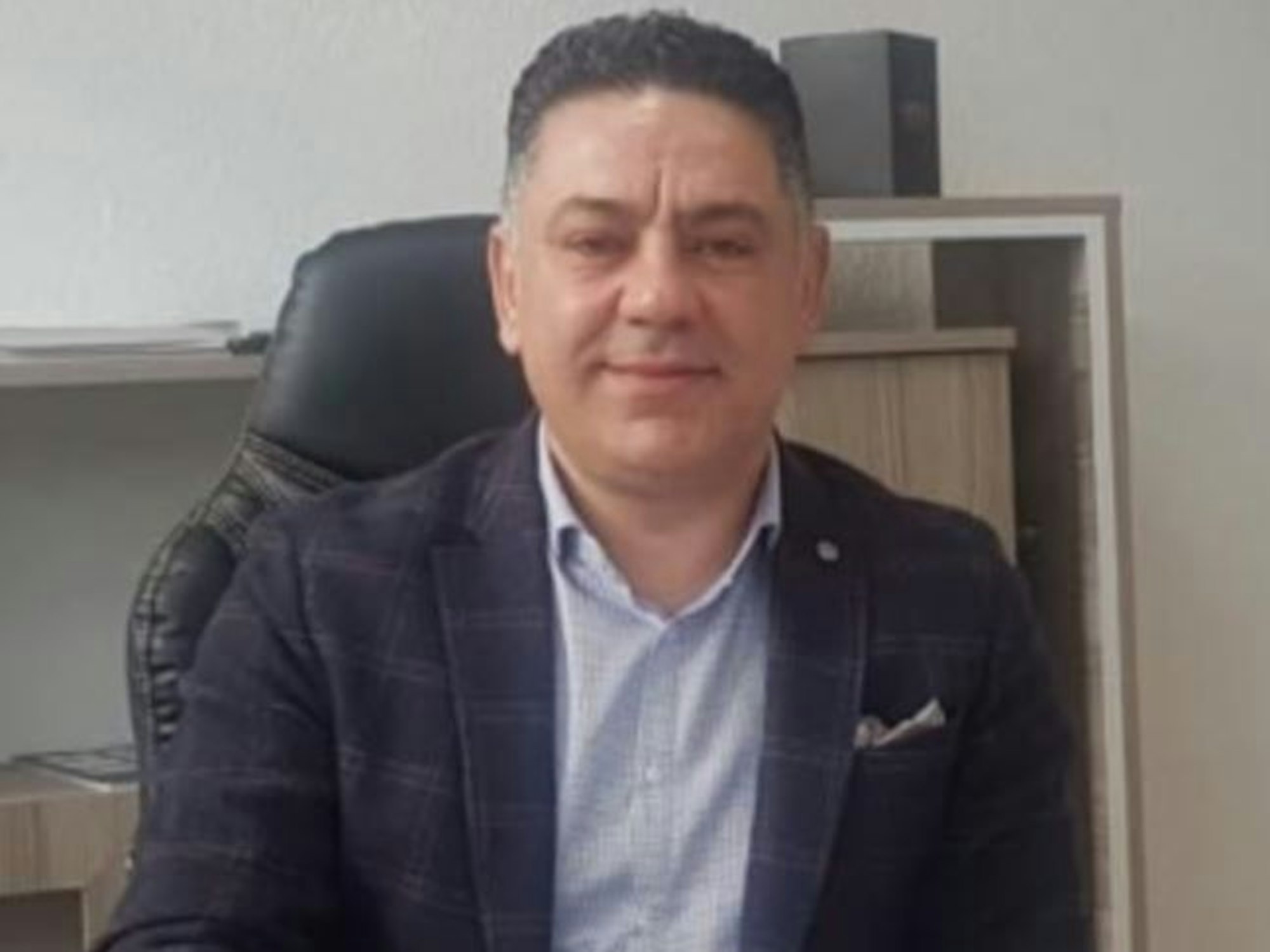 Fahndungsfoto: Ein Mann sitzt hinter einem Schreibtisch.