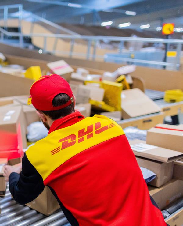 Ein Paketzusteller sortiert und räumt in einer Zustellbasis von Deutsche Post DHL Pakete in ein Zustellfahrzeug.