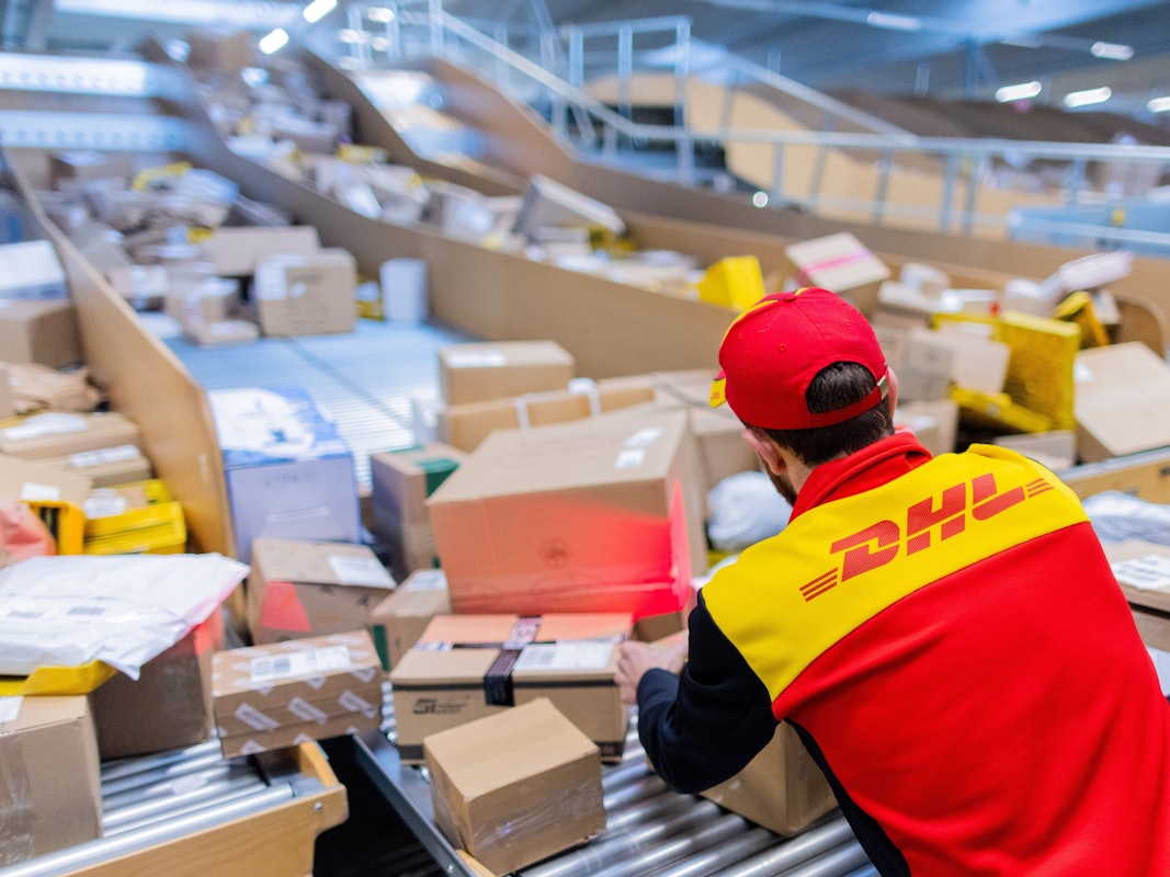 Ein Paketzusteller sortiert und räumt in einer Zustellbasis von Deutsche Post DHL Pakete in ein Zustellfahrzeug.