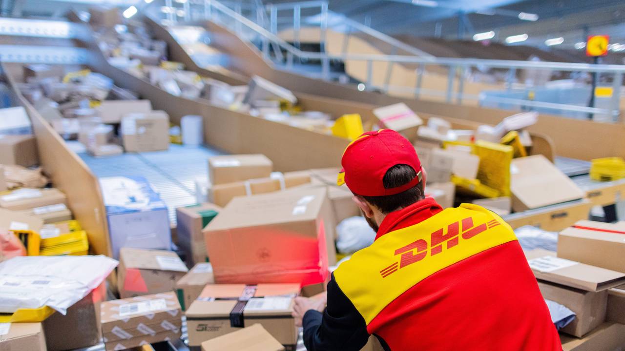 Ein Paketzusteller sortiert und räumt in einer Zustellbasis von Deutsche Post DHL Pakete in ein Zustellfahrzeug.
