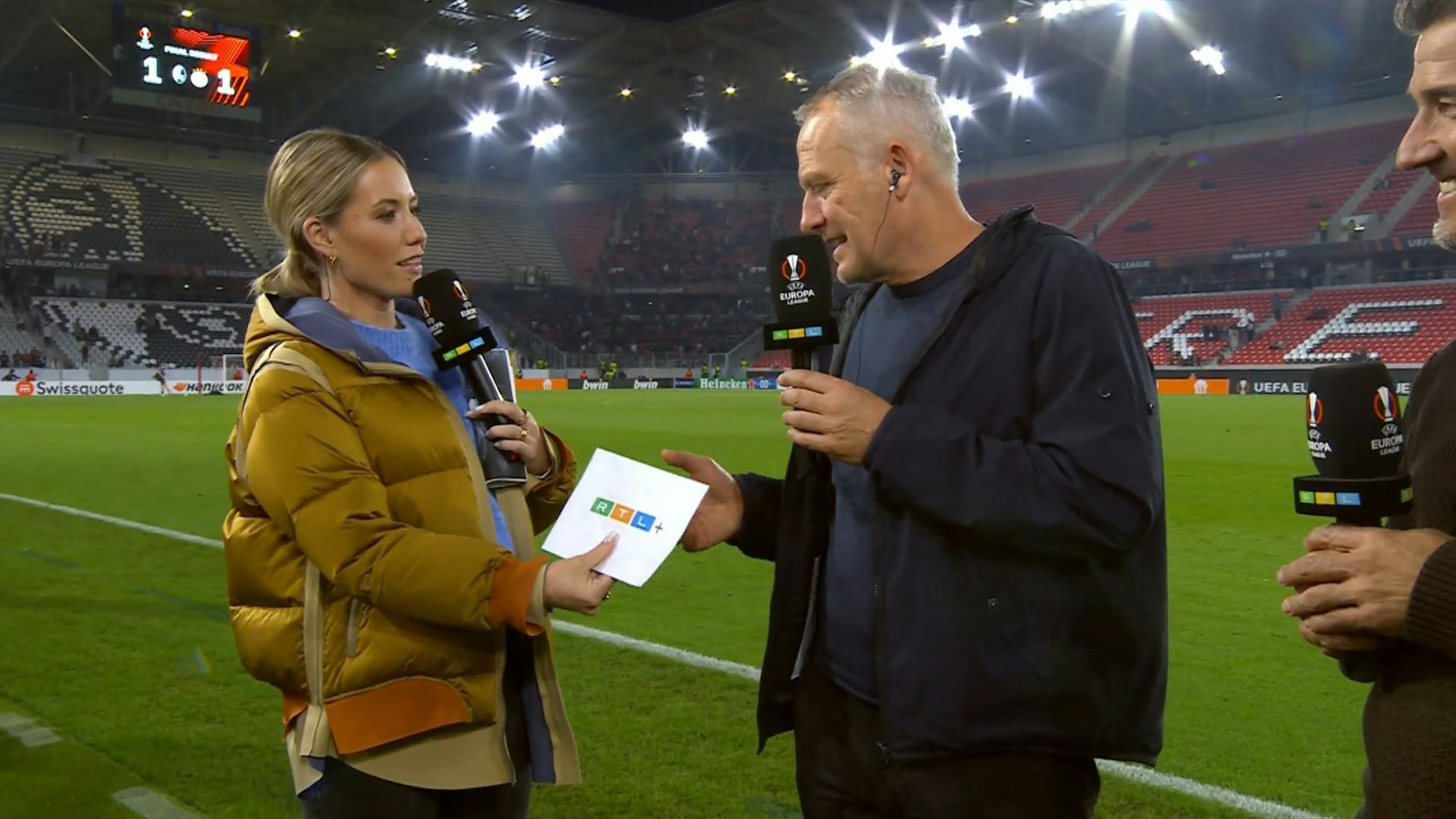 In Freiburg überreicht RTL-Moderatorin Laura Papendick SC-Trainer Christian Streich einen RTL+-Gutschein.