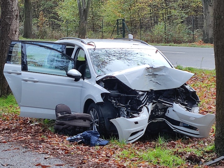 Ein Auto steht nach einem Baum-Aufprall stark beschädigt auf einem Grünstreifen.