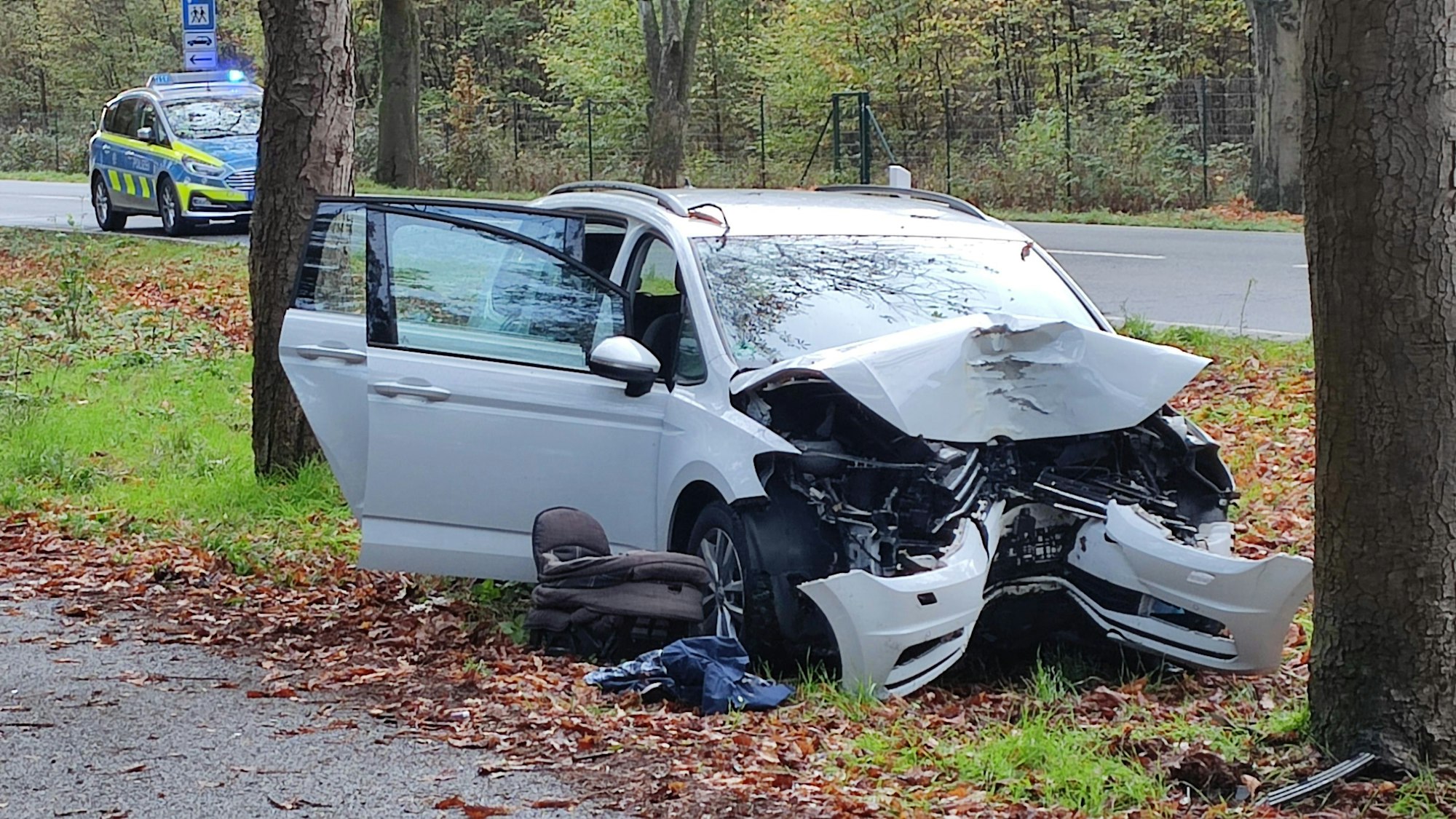 Ein Auto steht nach einem Baum-Aufprall stark beschädigt auf einem Grünstreifen.