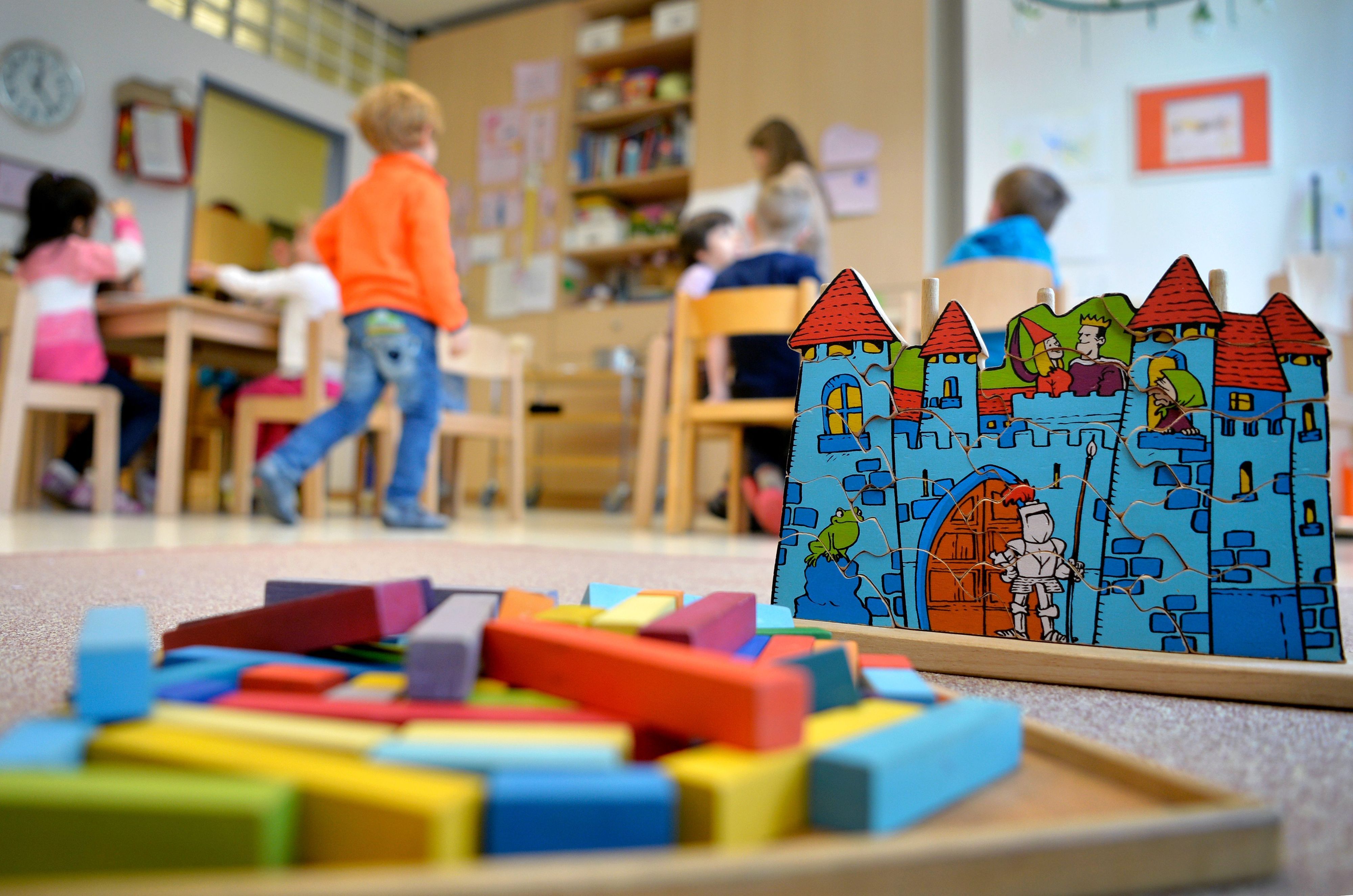 Bauklötze und ein Puzzle im Vordergrund, Kinder in einem Gruppenraum einer Kita im Hintergrund.