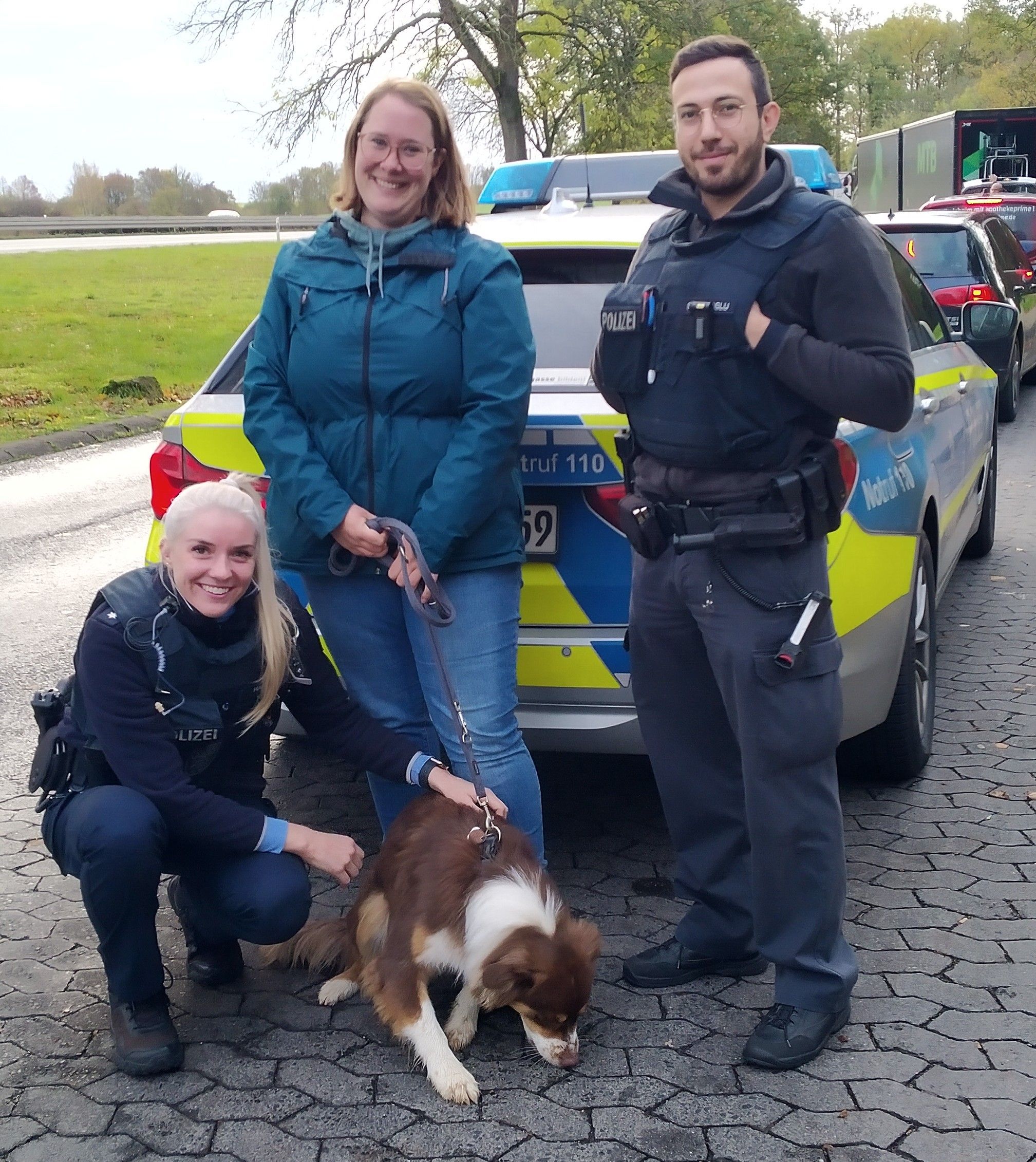 Die Besitzerin, eine Polizistin und ein Polizist lächeln nach der Übergabe der Hundin fröhlich in die Kamera.