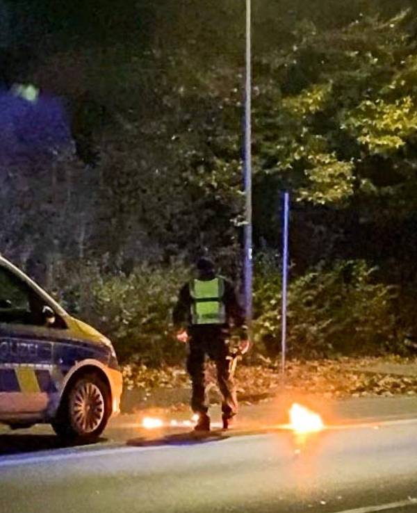 Ein Polizist steht am 4. November 2022 bei dem Feuer vor einem Streifenwagen. Bei einem Treffen der Tuning- und Raserszene an der A42 in Castrop-Rauxel (Kreis Recklinghausen) ist ein Mensch durch einen Knallkörper verletzt worden.