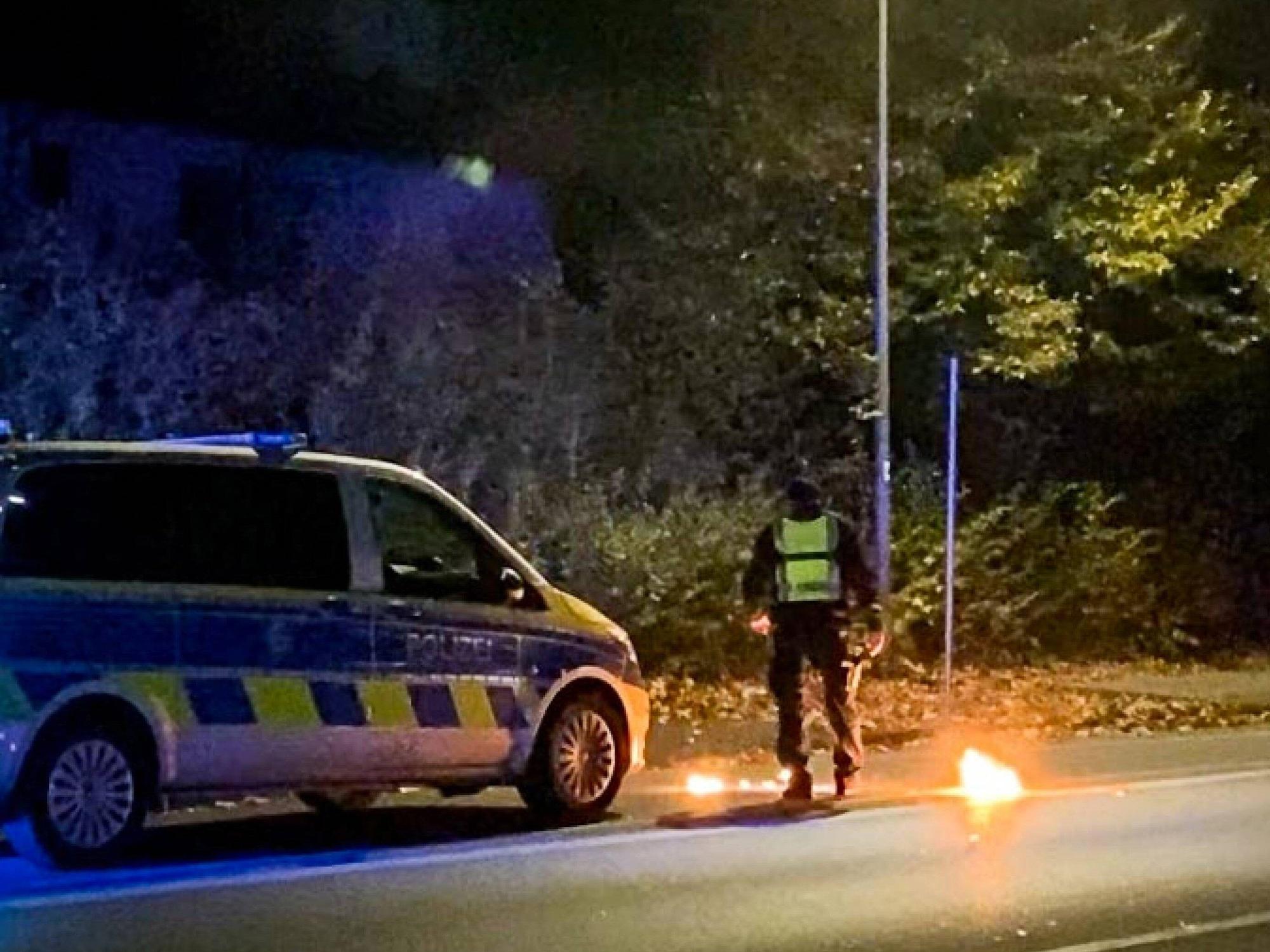 Ein Polizist steht am 4. November 2022 bei dem Feuer vor einem Streifenwagen. Bei einem Treffen der Tuning- und Raserszene an der A42 in Castrop-Rauxel (Kreis Recklinghausen) ist ein Mensch durch einen Knallkörper verletzt worden.
