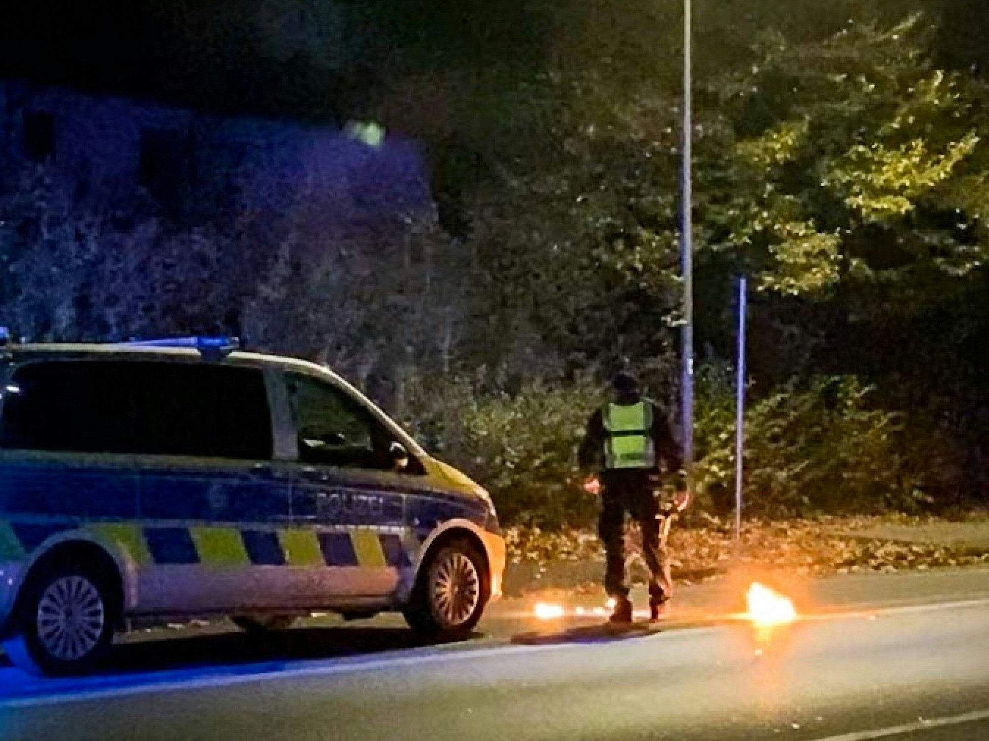 Ein Polizist steht am 4. November 2022 bei dem Feuer vor einem Streifenwagen. Bei einem Treffen der Tuning- und Raserszene an der A42 in Castrop-Rauxel (Kreis Recklinghausen) ist ein Mensch durch einen Knallkörper verletzt worden.