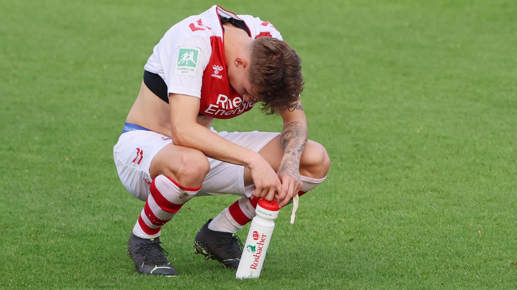 Simon Breuer kniet nach einem Spiel der U21 des 1. FC Köln enttäuscht auf dem Rasen.