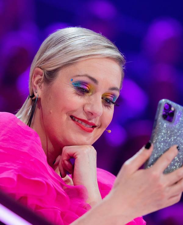 Ruth Moschner aus dem Rateteam sitzt am Ratepult im Finale der ProSieben-Show „The Masked Singer“ und blickt auf ihr Handy.
