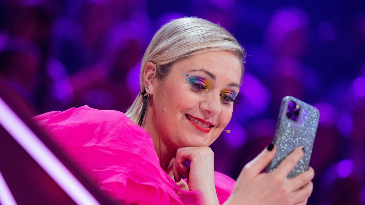 Ruth Moschner aus dem Rateteam sitzt am Ratepult im Finale der ProSieben-Show „The Masked Singer“ und blickt auf ihr Handy.