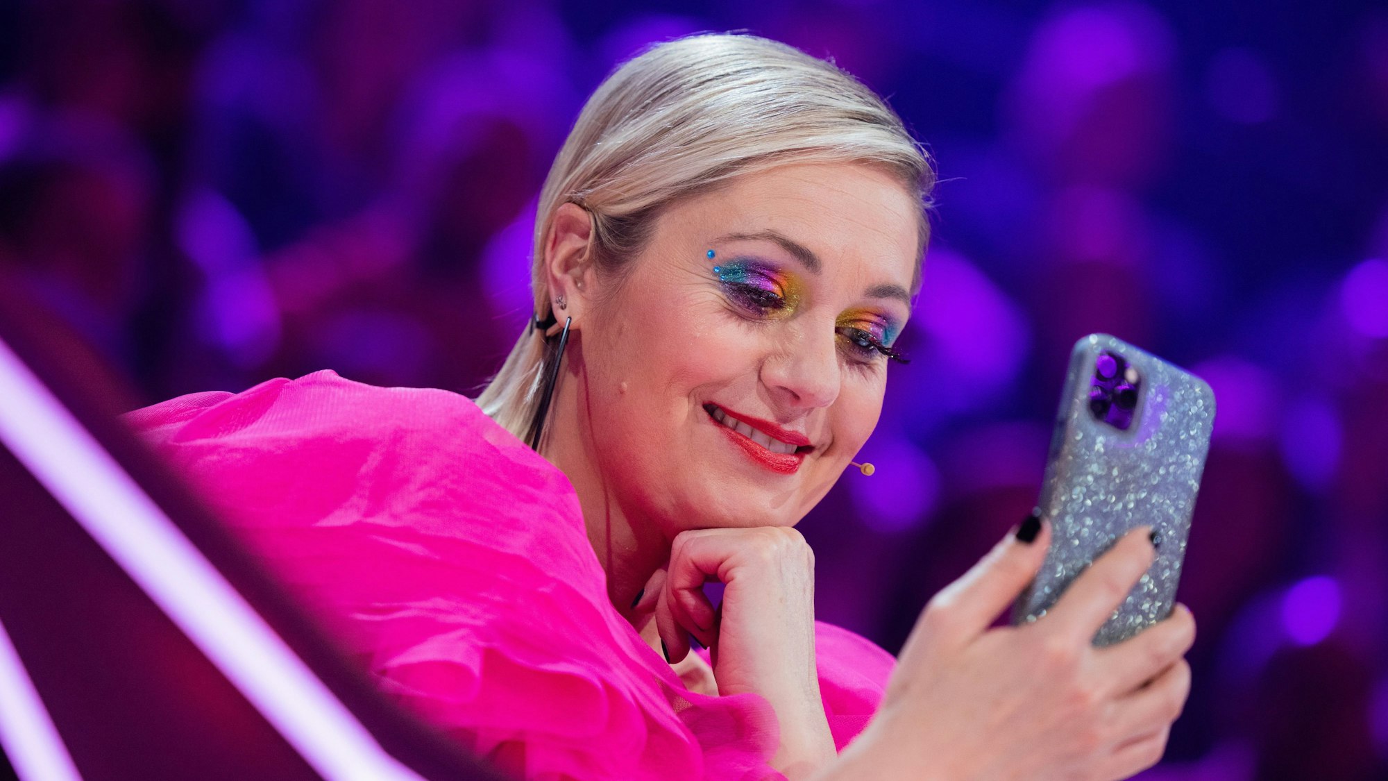 Ruth Moschner aus dem Rateteam sitzt am Ratepult im Finale der ProSieben-Show „The Masked Singer“ und blickt auf ihr Handy.