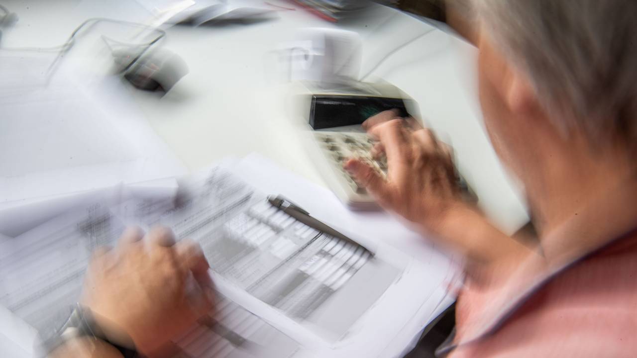 Ein Rentner füllt seine Steuererklärung aus und tippt zur Berechnung Zahlen in einen Tischrechner.