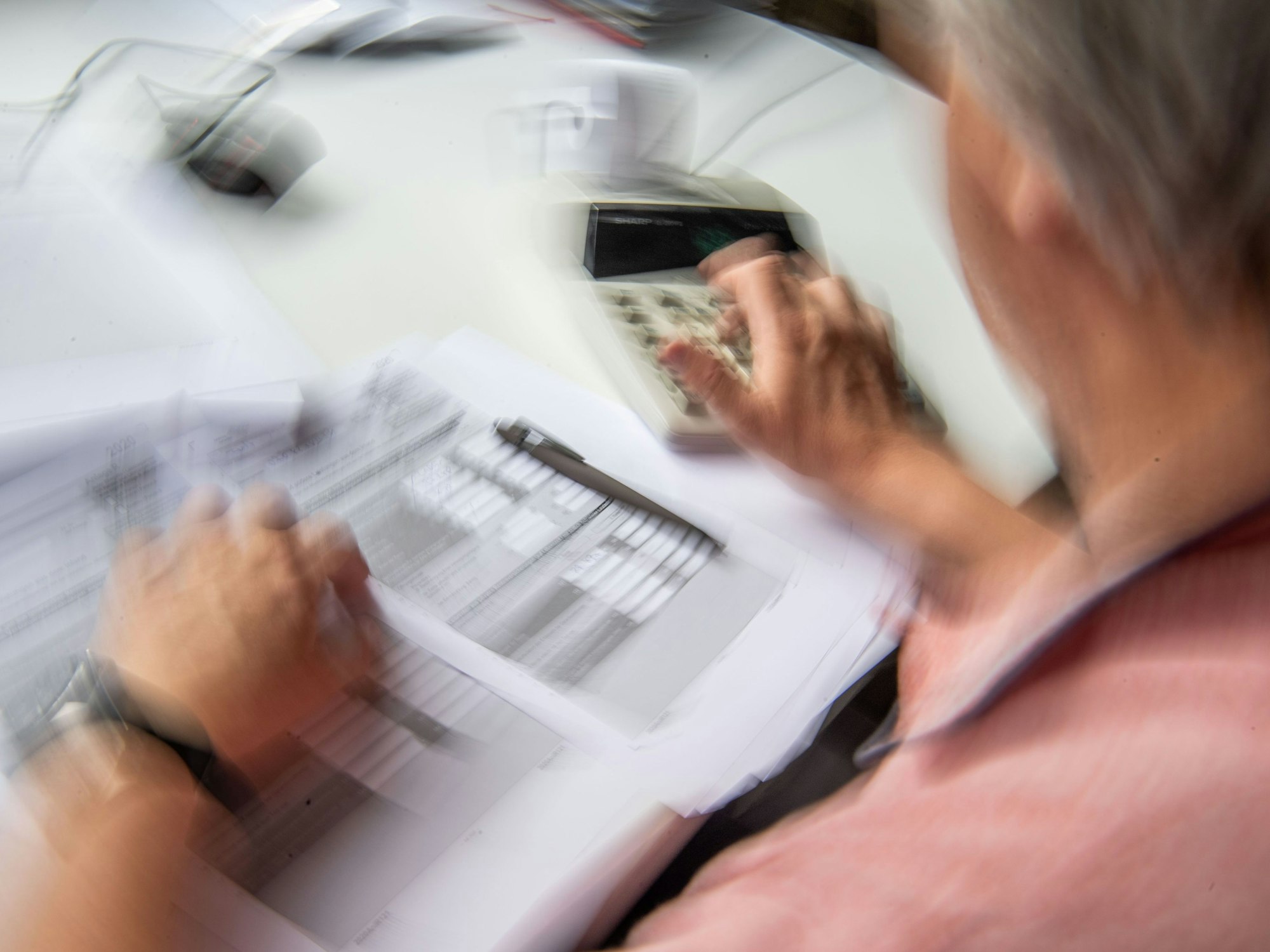 Ein Rentner füllt seine Steuererklärung aus und tippt zur Berechnung Zahlen in einen Tischrechner.