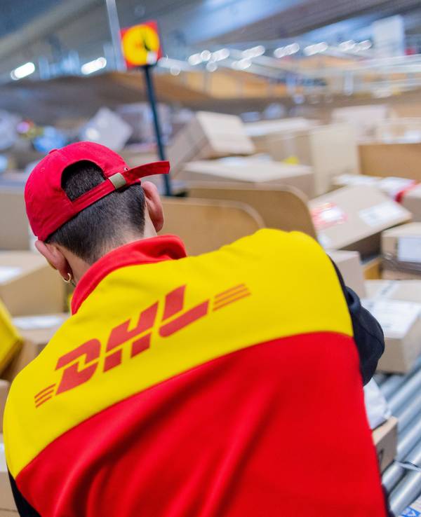 Ein Paketzusteller sortiert und räumt in einer Zustellbasis von Deutsche Post DHL Pakete in ein Zustellfahrzeug.