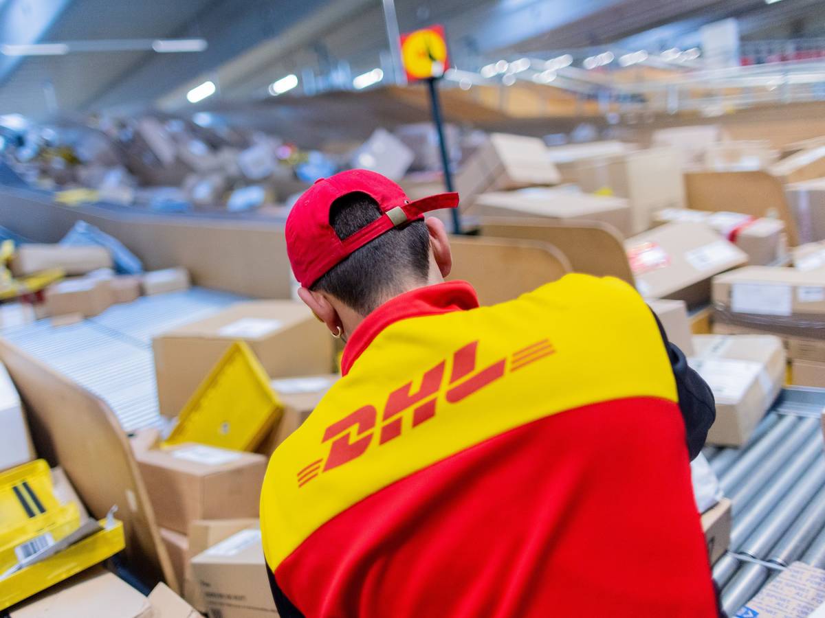 Ein Paketzusteller sortiert und räumt in einer Zustellbasis von Deutsche Post DHL Pakete in ein Zustellfahrzeug.