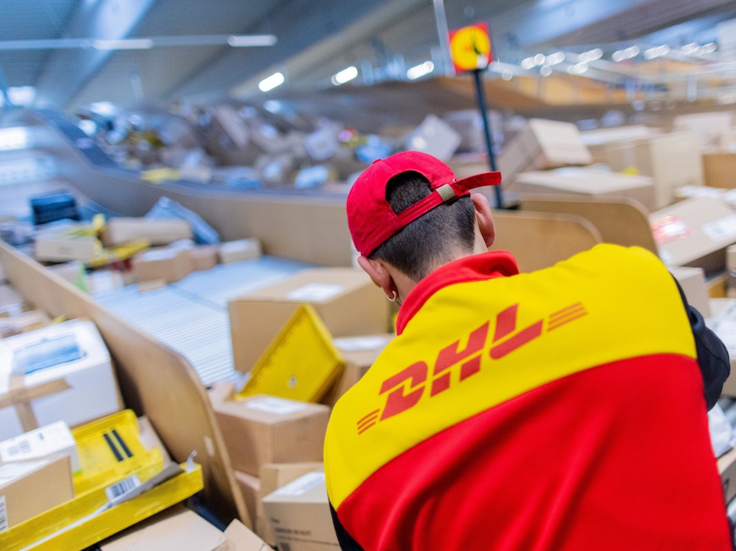 Ein Paketzusteller sortiert und räumt in einer Zustellbasis von Deutsche Post DHL Pakete in ein Zustellfahrzeug.