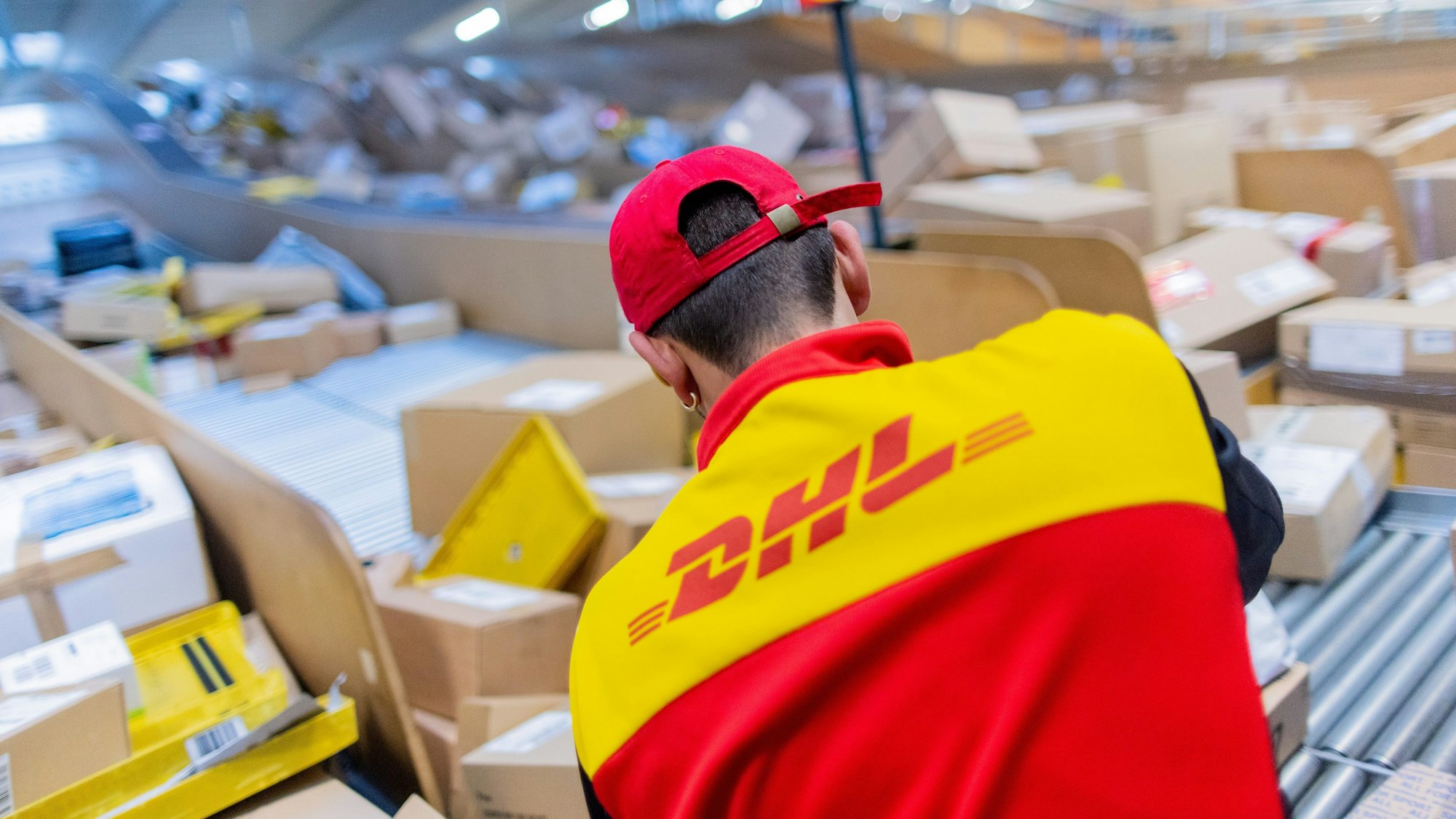 Ein Paketzusteller sortiert und räumt in einer Zustellbasis von Deutsche Post DHL Pakete in ein Zustellfahrzeug.