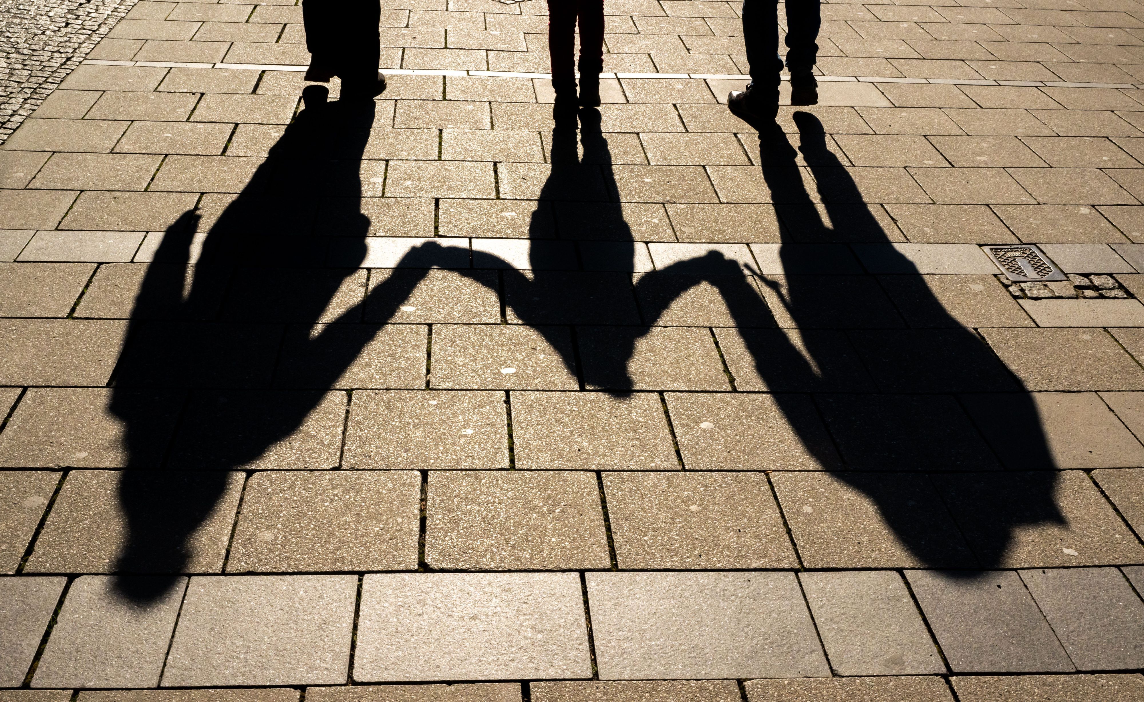 Die Schatten von zwei Erwachsenen und einem Kind fallen in den Morgenstunden auf den Asphalt.