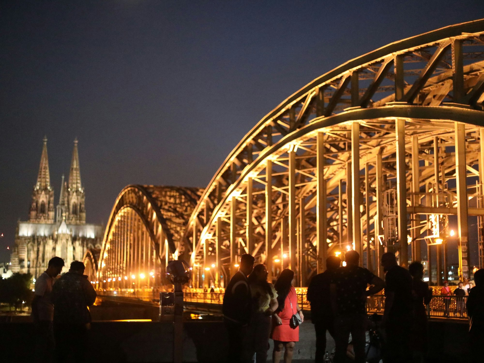 Menschen posieren bei Nacht vor dem Kölner Dom und der Hohenzollernbrücke am Rheinboulevard in Deutz.