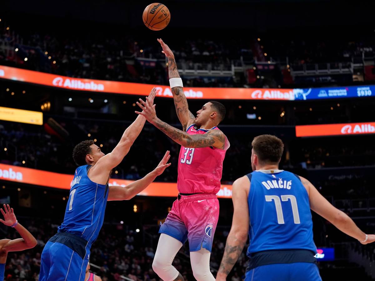 Washington Wizards Kyle Kuzma (m.) springt hoch, um einen Treffer zu erzielen, Mavericks Spencer Dinwiddie versucht ihn daran zu hindern.