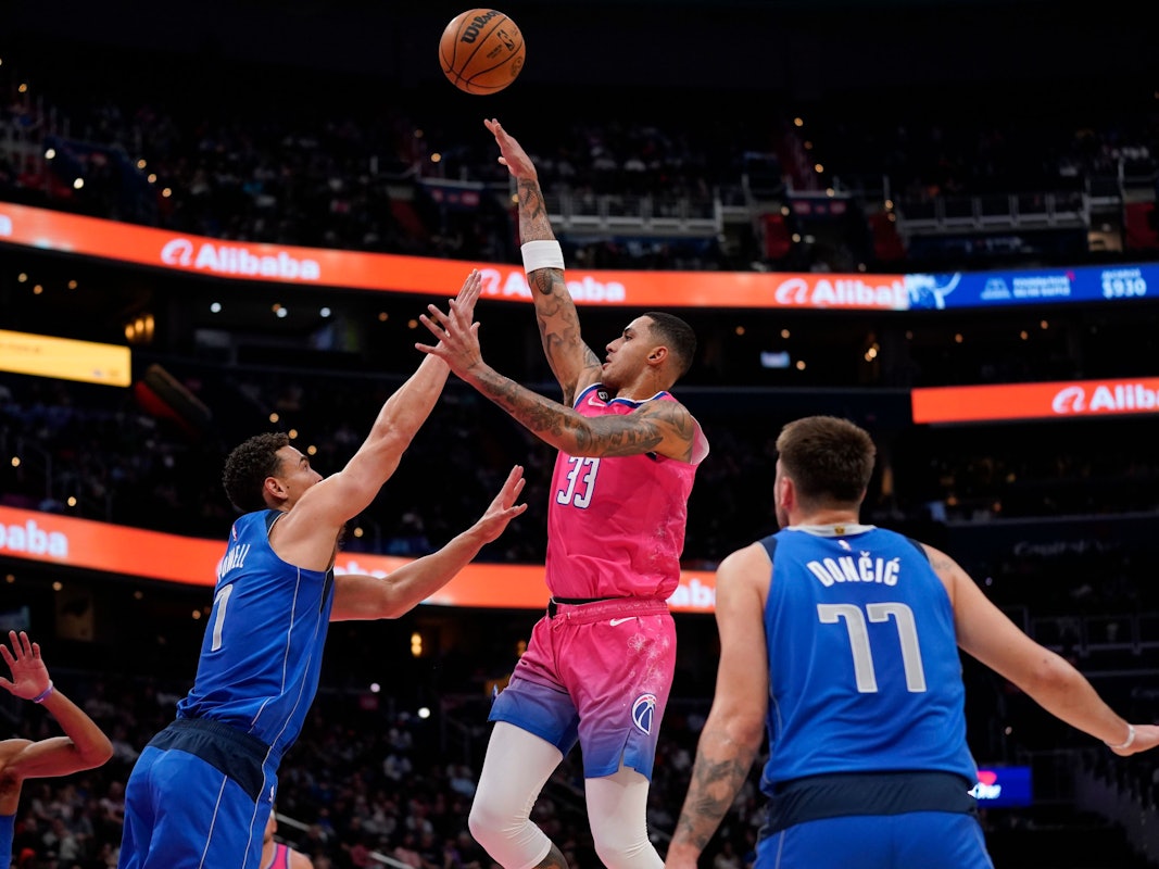 Washington Wizards Kyle Kuzma (m.) springt hoch, um einen Treffer zu erzielen, Mavericks Spencer Dinwiddie versucht ihn daran zu hindern.