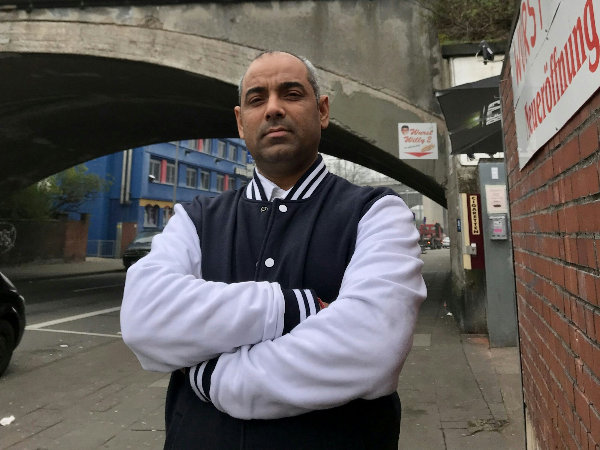 Sanjeev Sharma steht mit verschränkten Armen vor einer Unterführung in Köln und guckt in die Kamera.