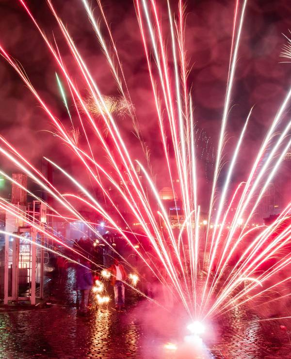 Menschen stehen auf einem Platz, auf dem Feuerwerk explodiert.