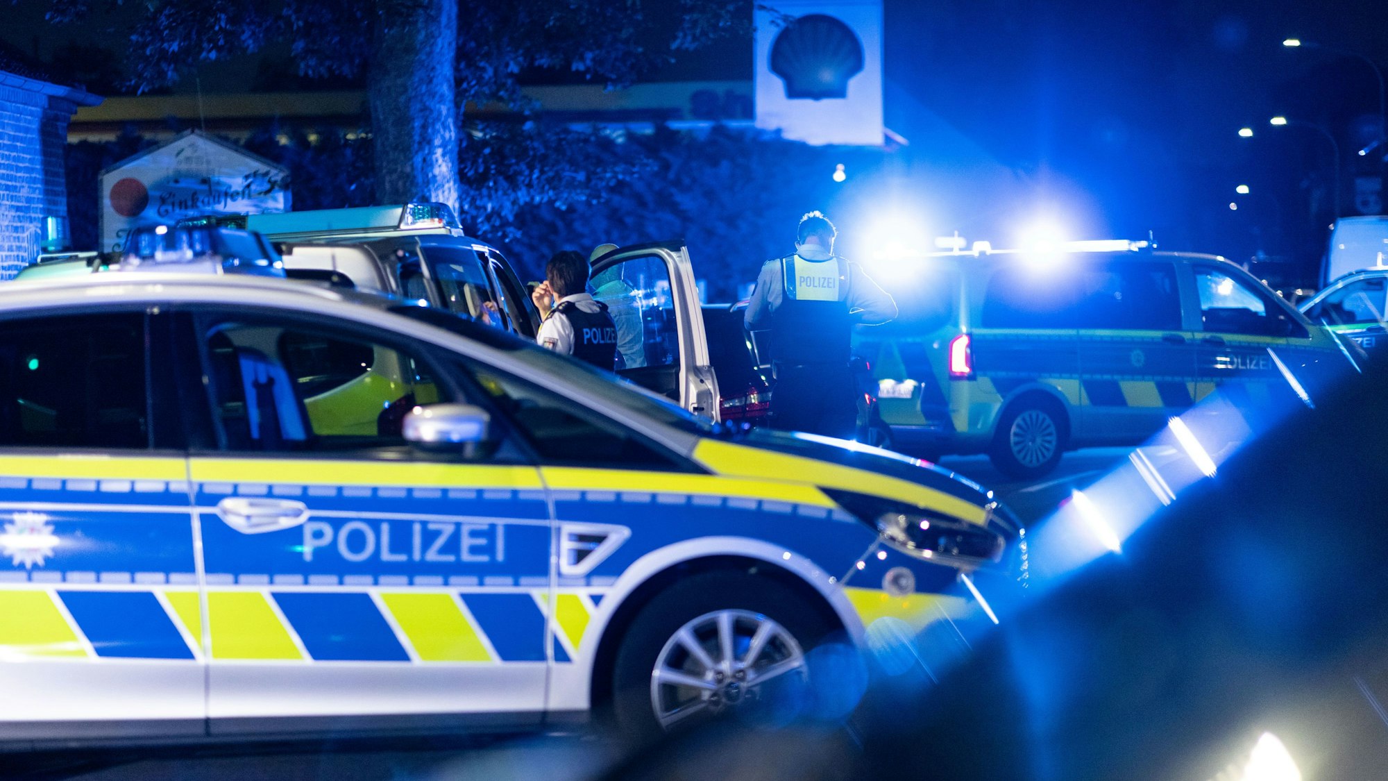 Einsatzkräfte der Polizei stehen vor einer Tankstelle.
