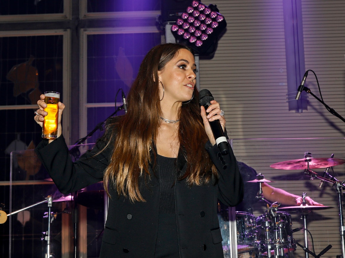 Vanessa Mai steht mit Bierglas und Mikrofon in der Hand auf der Bühne der Blauen Funken in Köln.