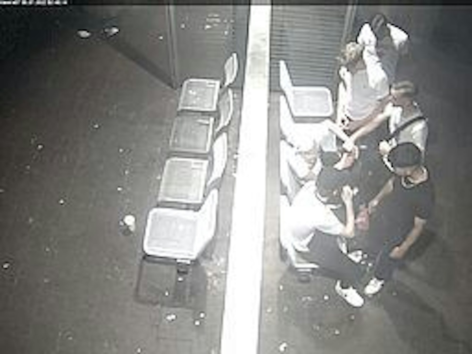 Vier junge Männer stehen vor zwei Männern, die sich gegen sie wehren wollen. Das Foto ist von oben aufgenommen und stammt aus einer Überwachungskamera.