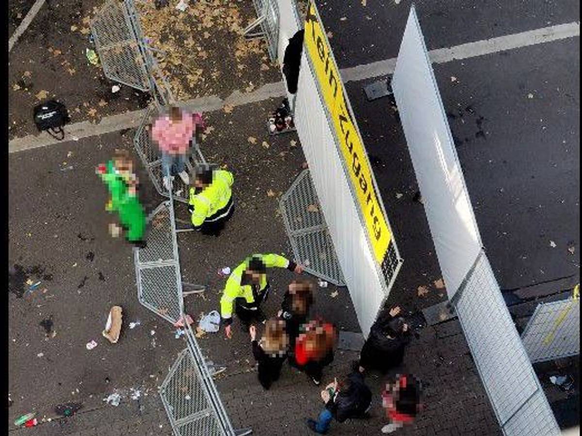 Zwei Mitarbeiter des Sicherheitsdienstes sprechen an einer Absperrung mit kostümierten Personen.