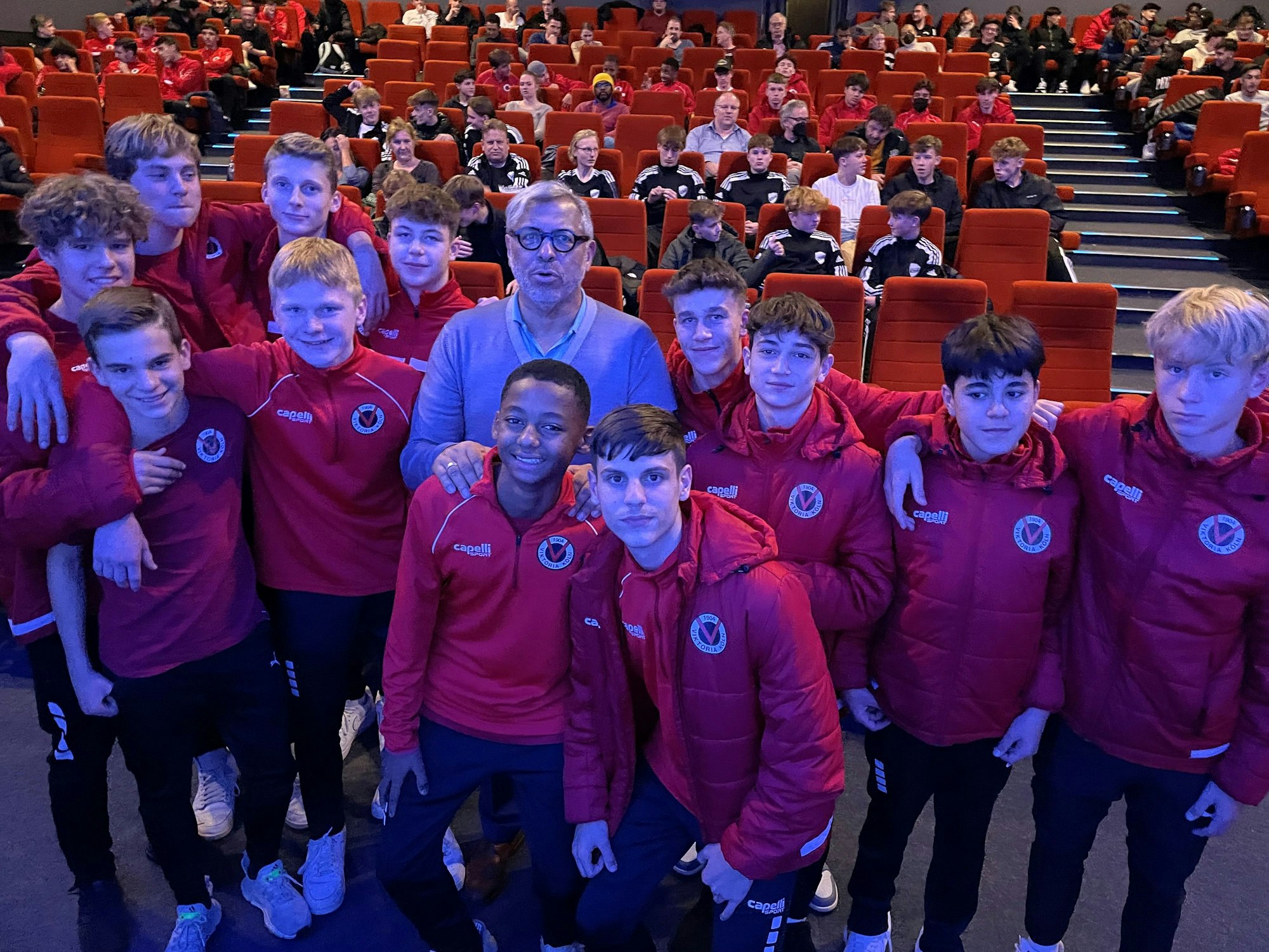 Jimmy Hartwig steht mit Nachwuchsspielern von Viktoria Köln zusammen im Kino.